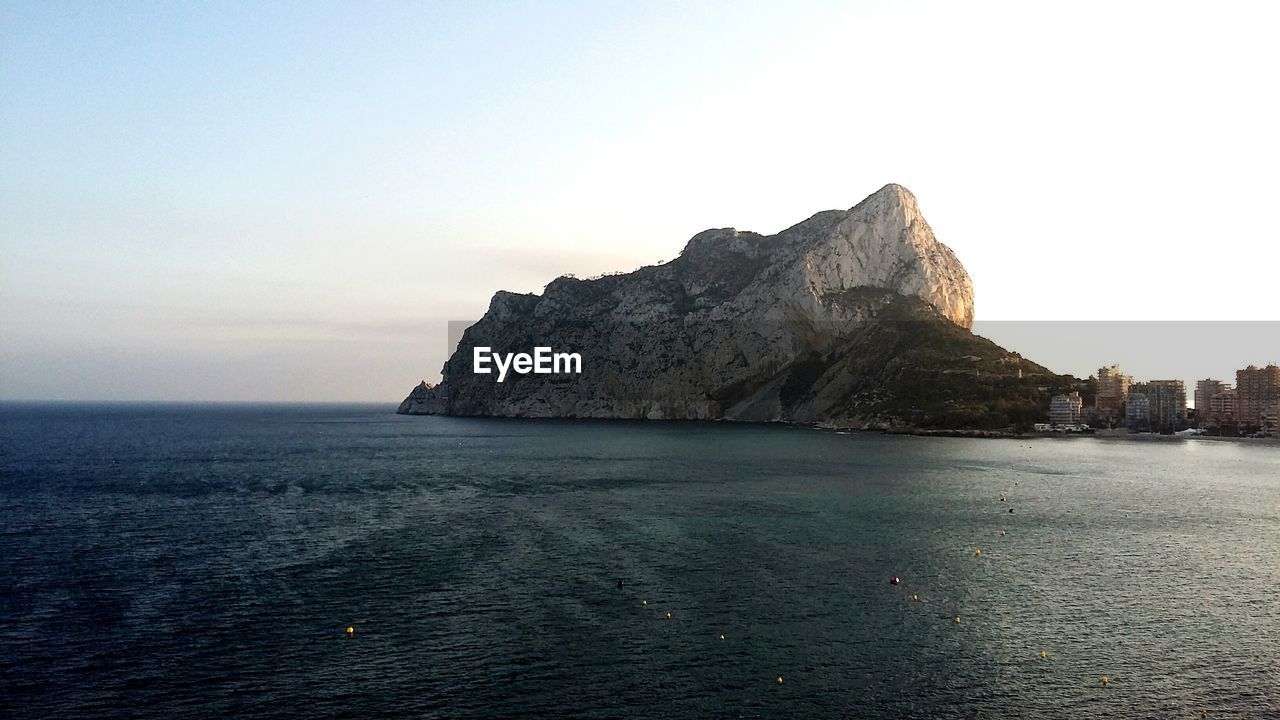 VIEW OF CALM SEA AGAINST ROCKY MOUNTAIN