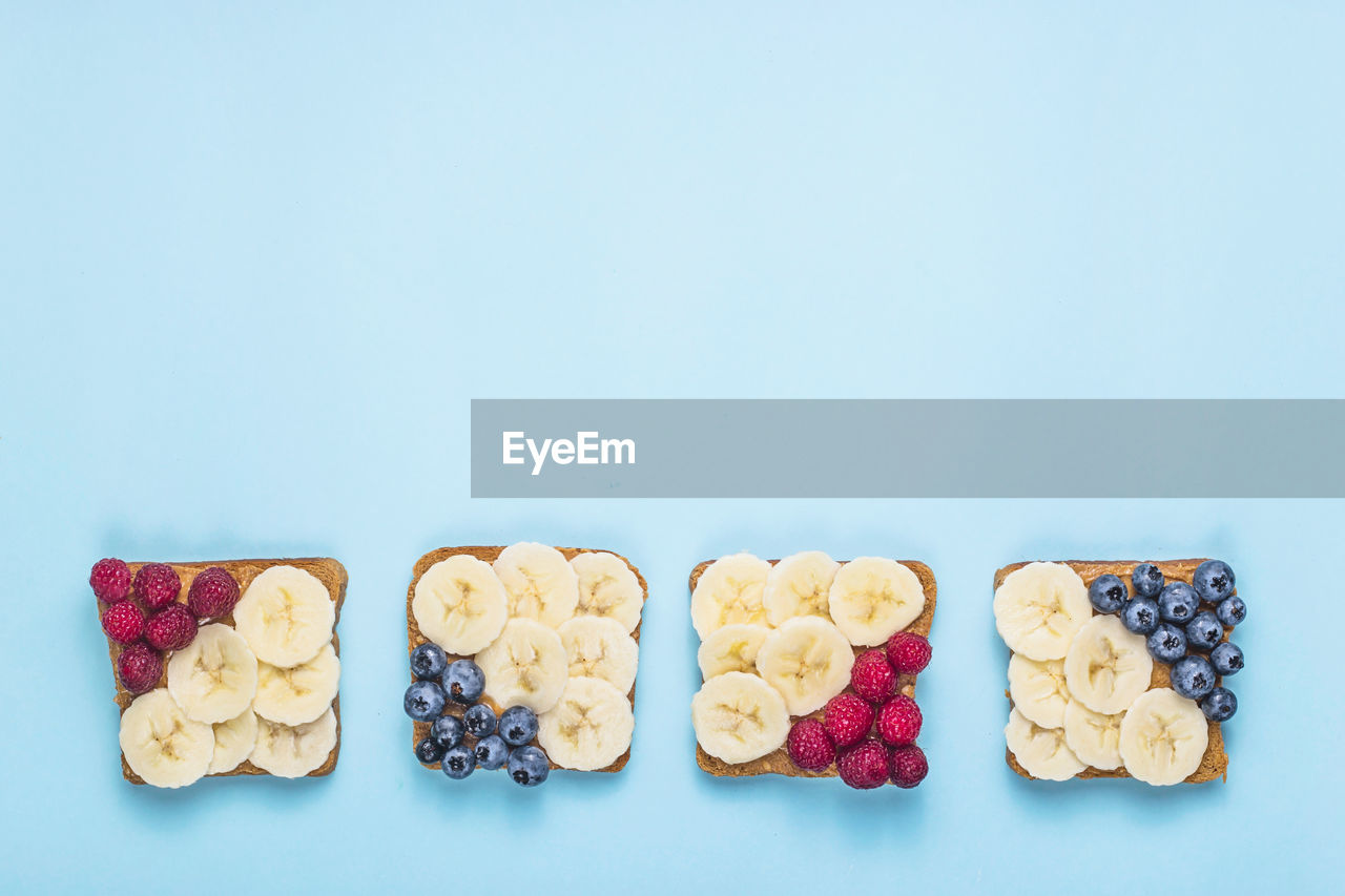 Healthy breakfast of sandwiches with peanut butter, banana and berries on a bright blue background. 