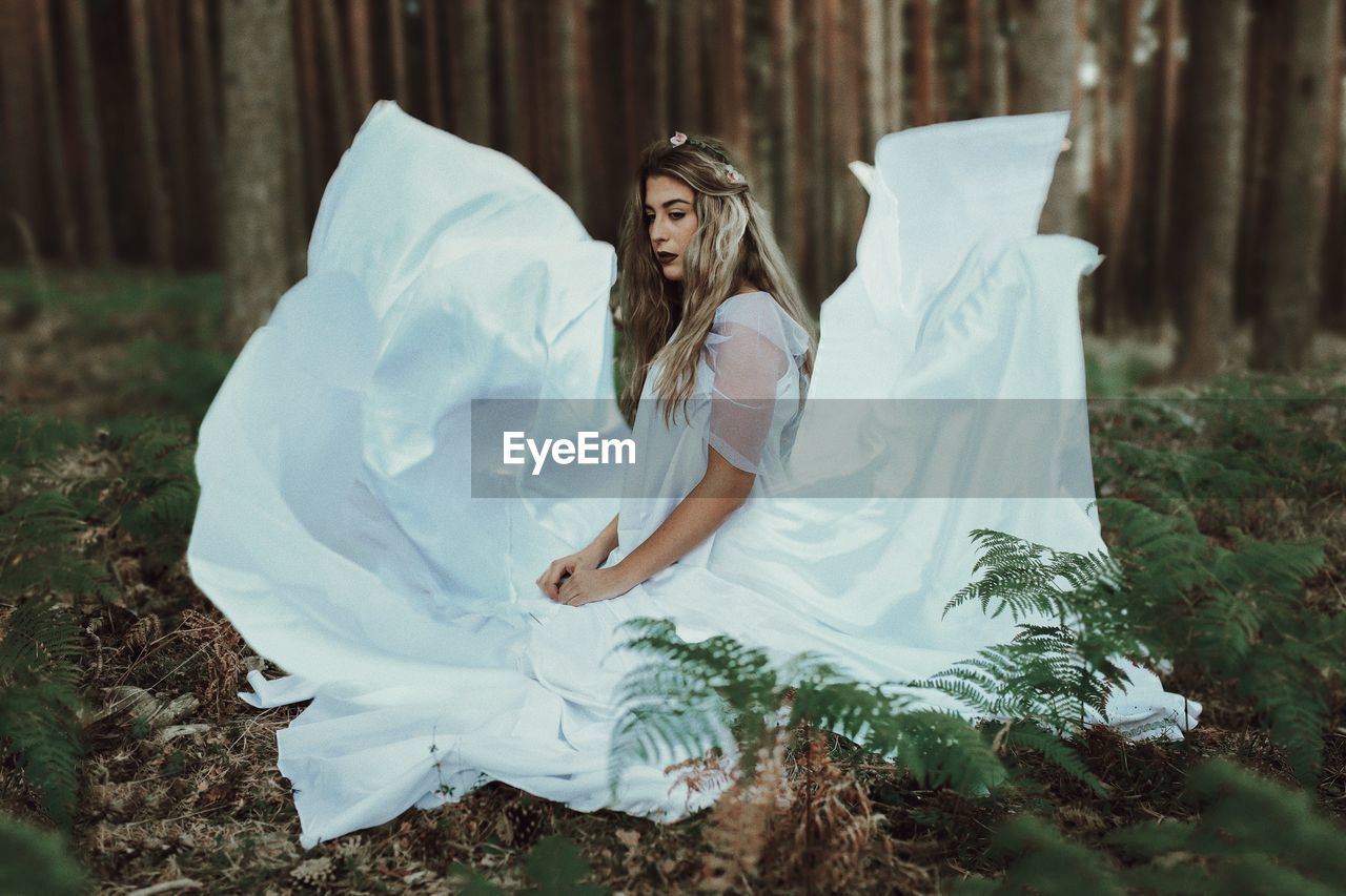 Side view of young woman in dress sitting at forest