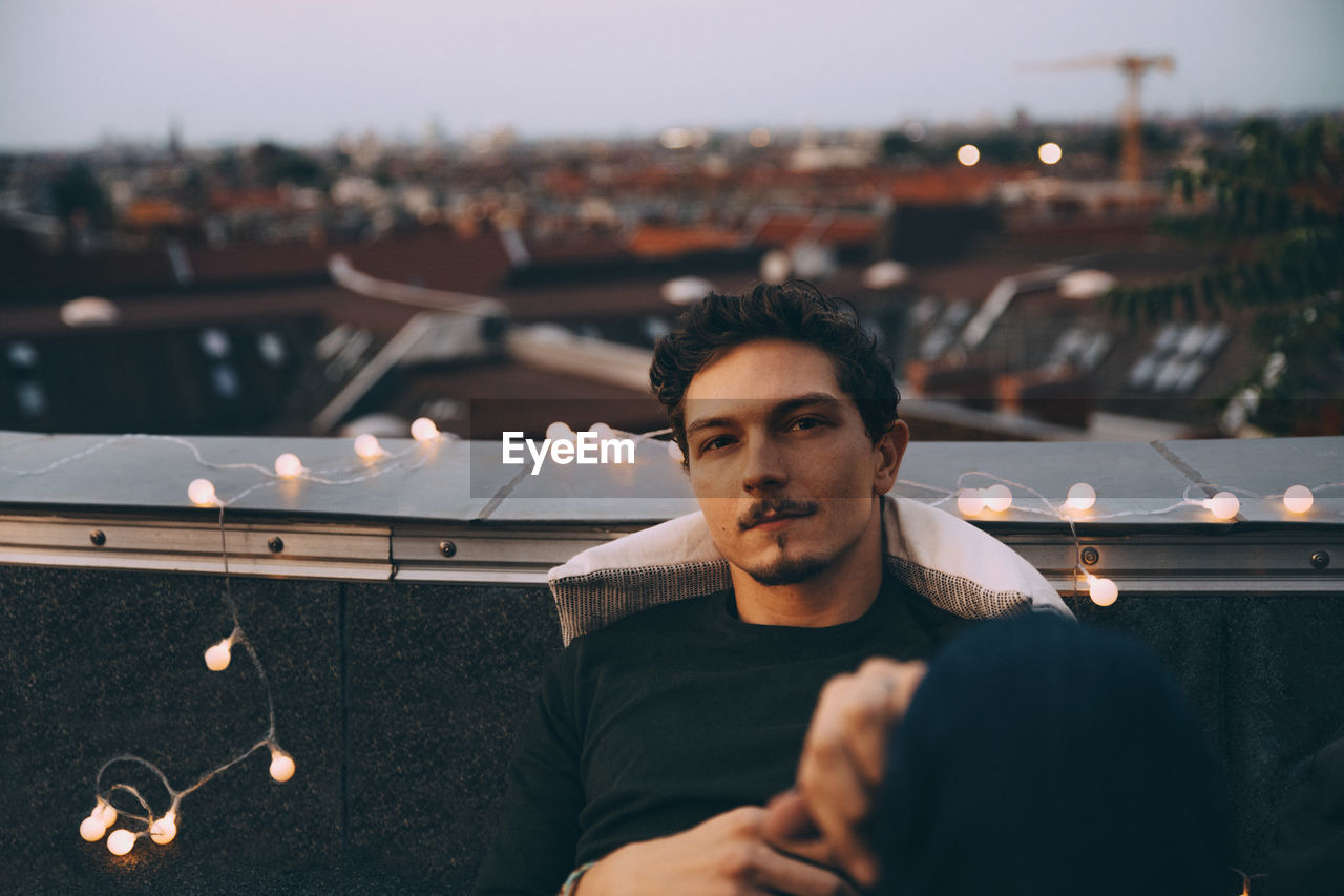 Portrait of young man sitting on illuminated terrace in city during party