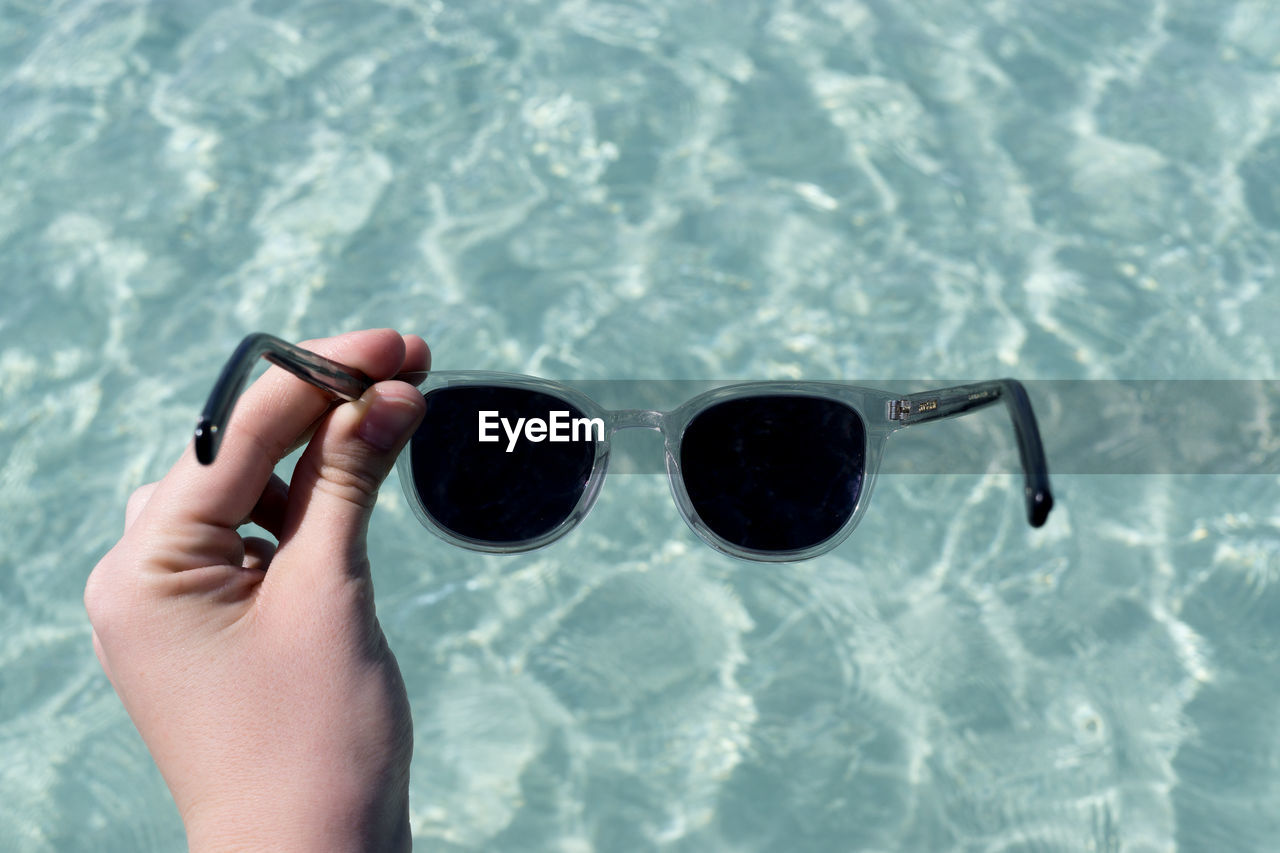 Cropped hand of woman holding sunglasses over swimming pool