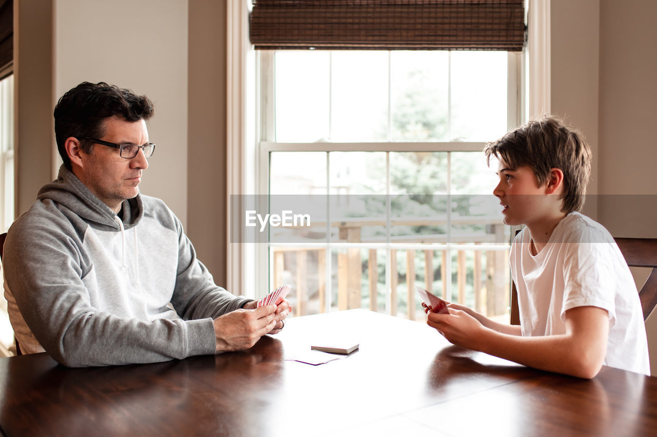 Adolescent boy and his father playing cards at the table together.