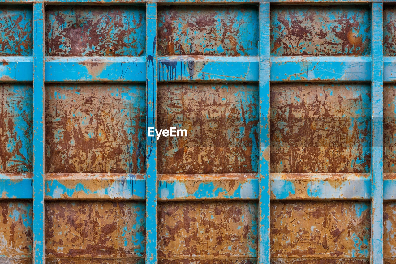 Rusted reinforced container wall with leftovers of blue paint, flat full-frame background and
