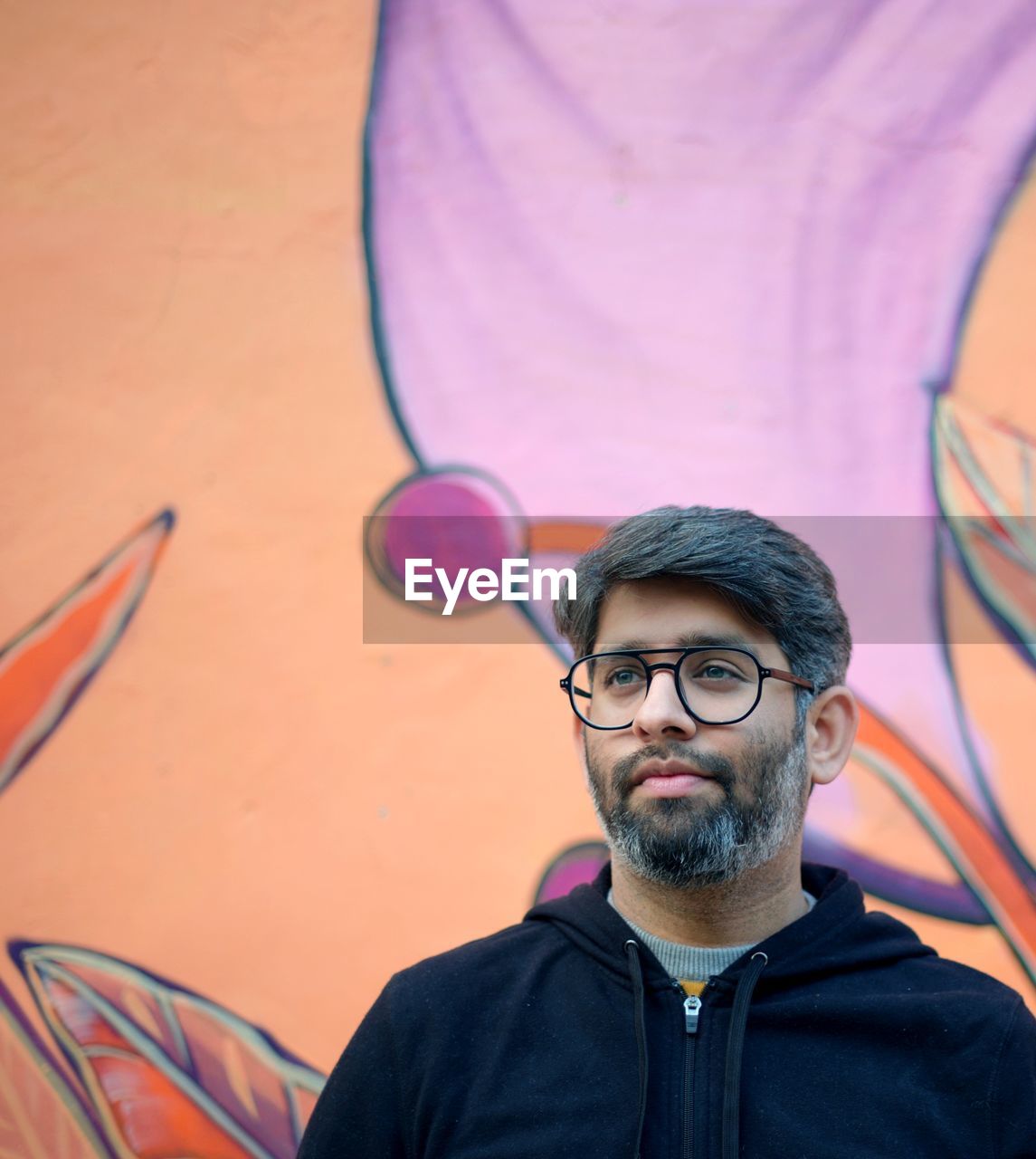 Man wearing eyeglasses looking away while standing against wall outdoors