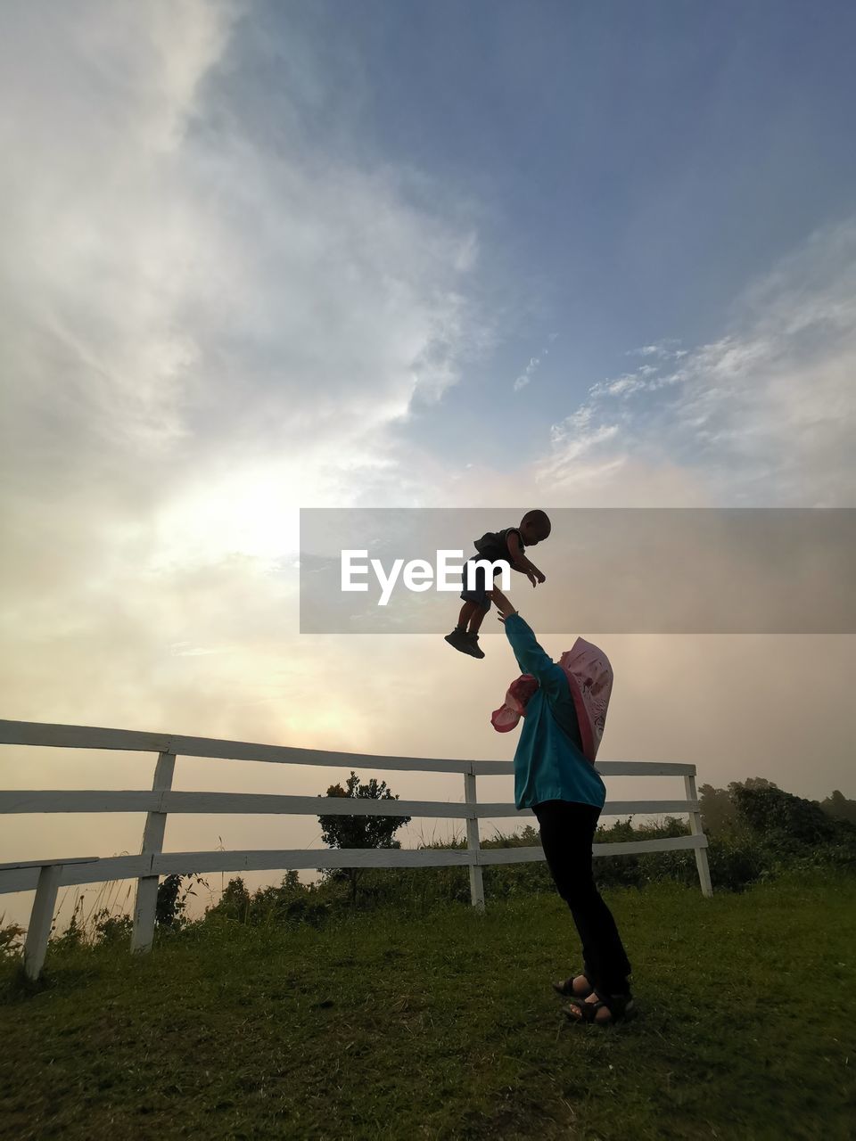 FULL LENGTH OF WOMAN STANDING ON FIELD AGAINST SKY AT SUNSET