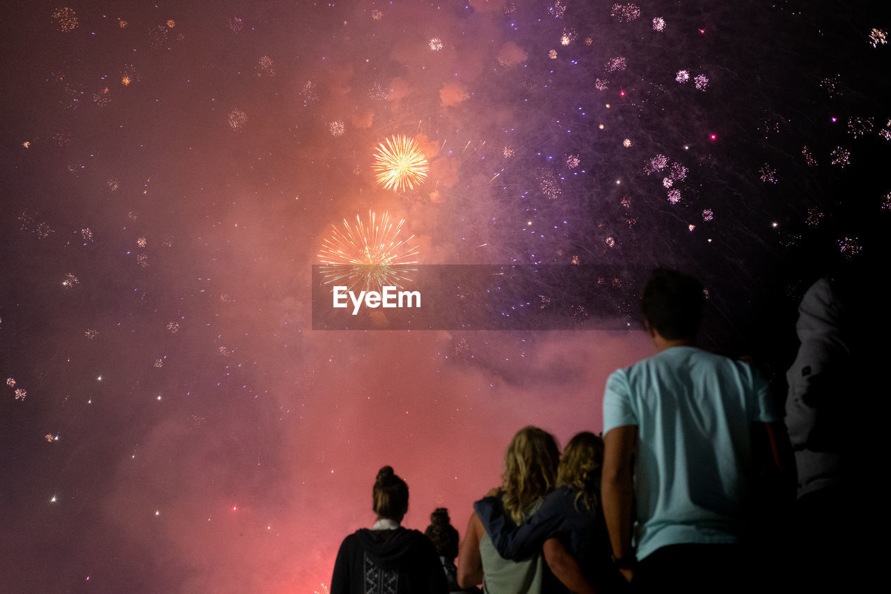 Rear view of people looking at fireworks against sky at night