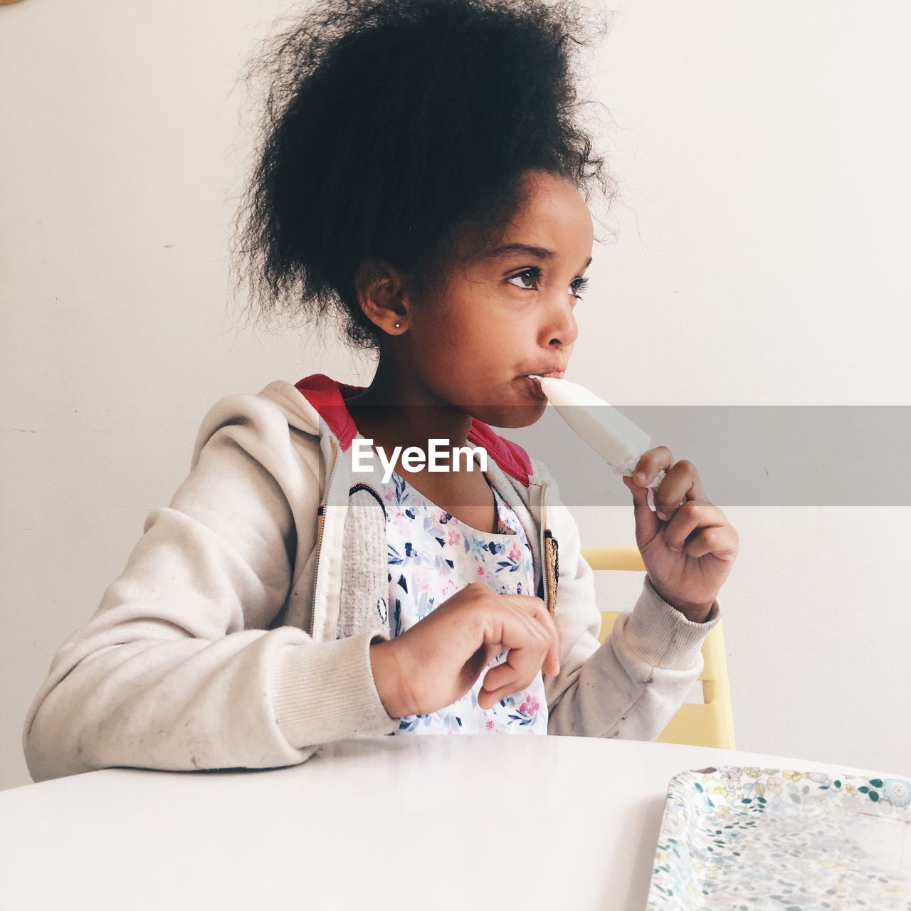 Girl eating popsicle against wall at home