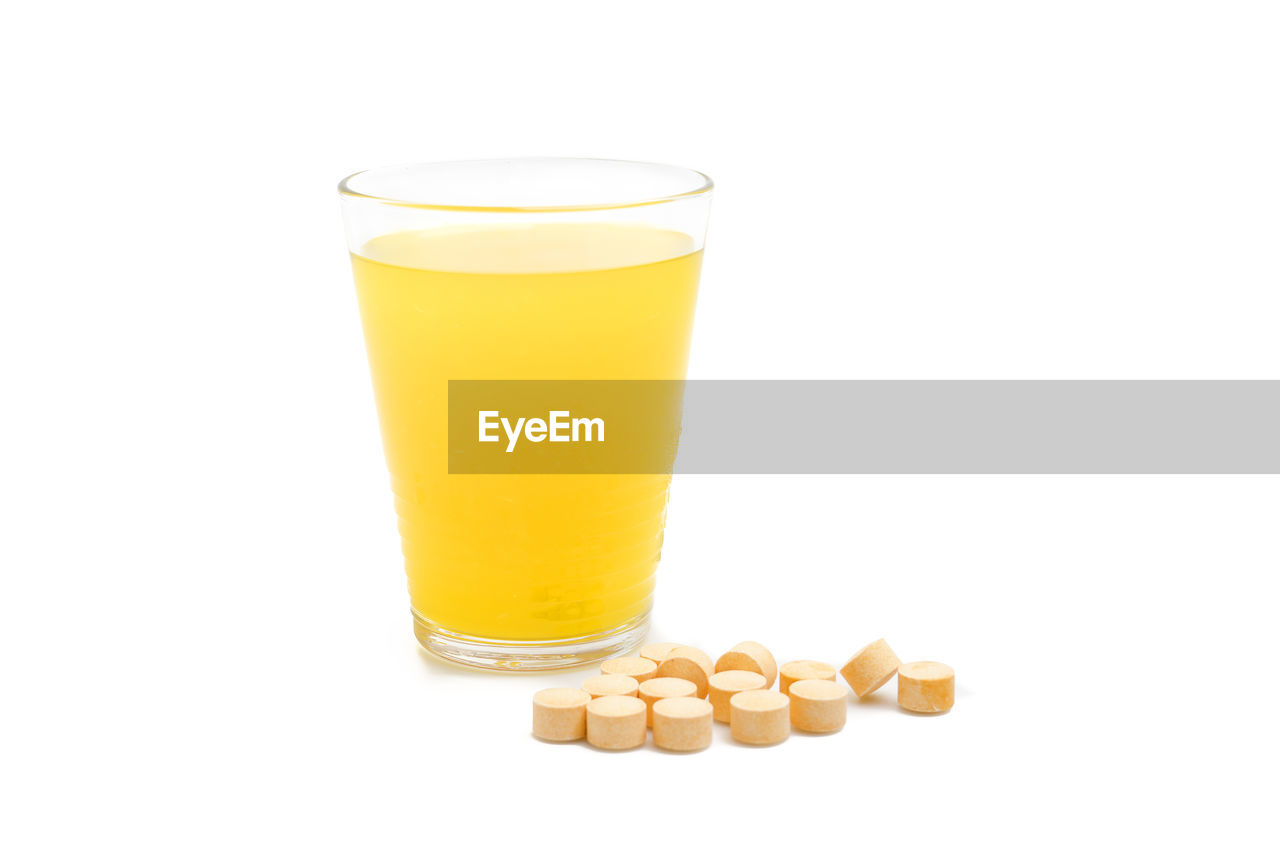 Glass on orange juice and vitamin c tablets on white background.