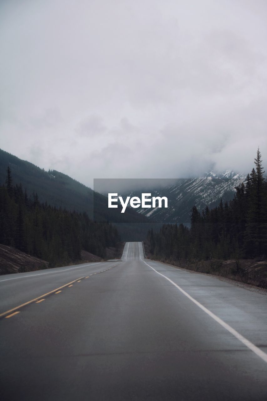 Road leading towards mountain against cloudy sky