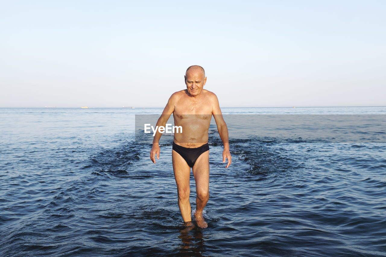 Shirtless man wading in sea against sky