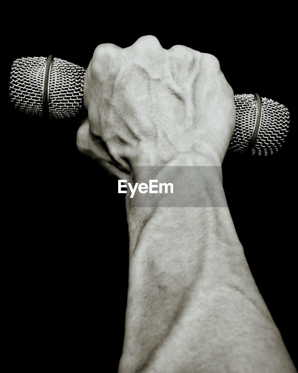 Close-up of man hand holding microphones against black background