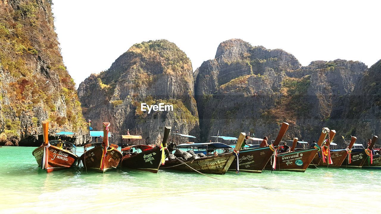Longtail boats moored at beach against rocky mountains at halong bay