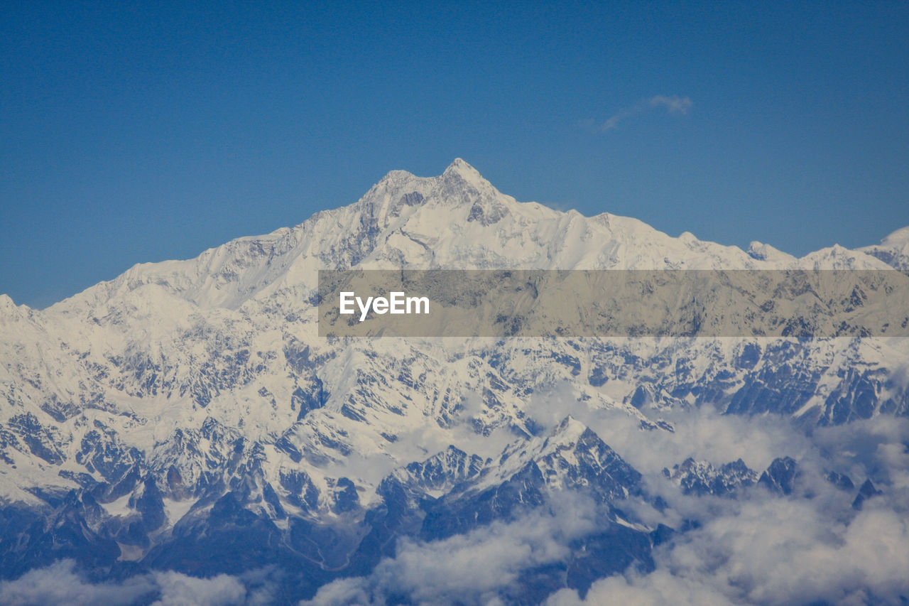 Low angle view of snowcapped mountains against clear blue sky