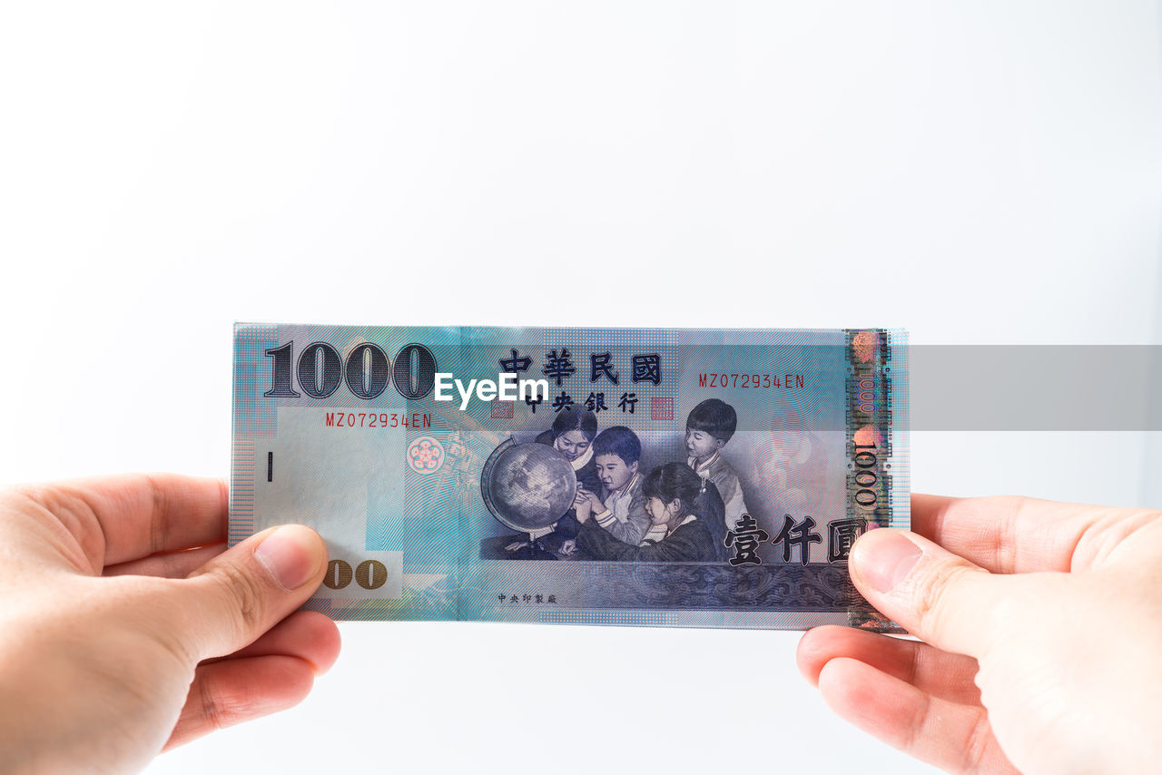 cropped hand of person holding paper currency against white background