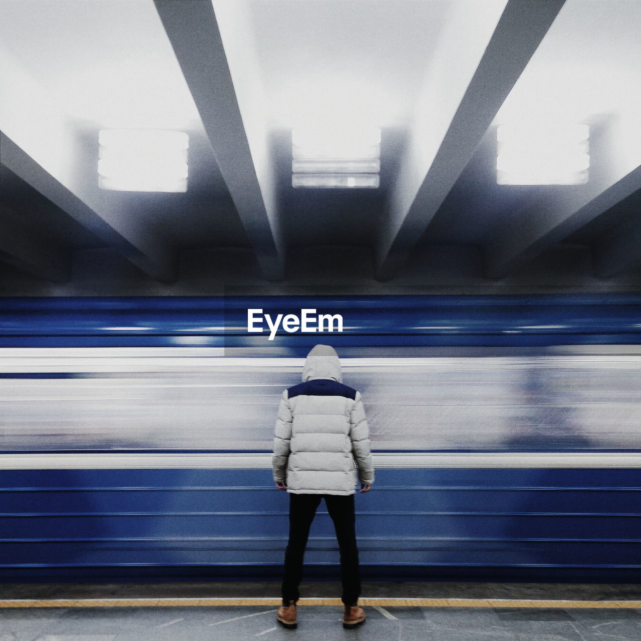 Rear view of man standing against train moving at illuminated subway station