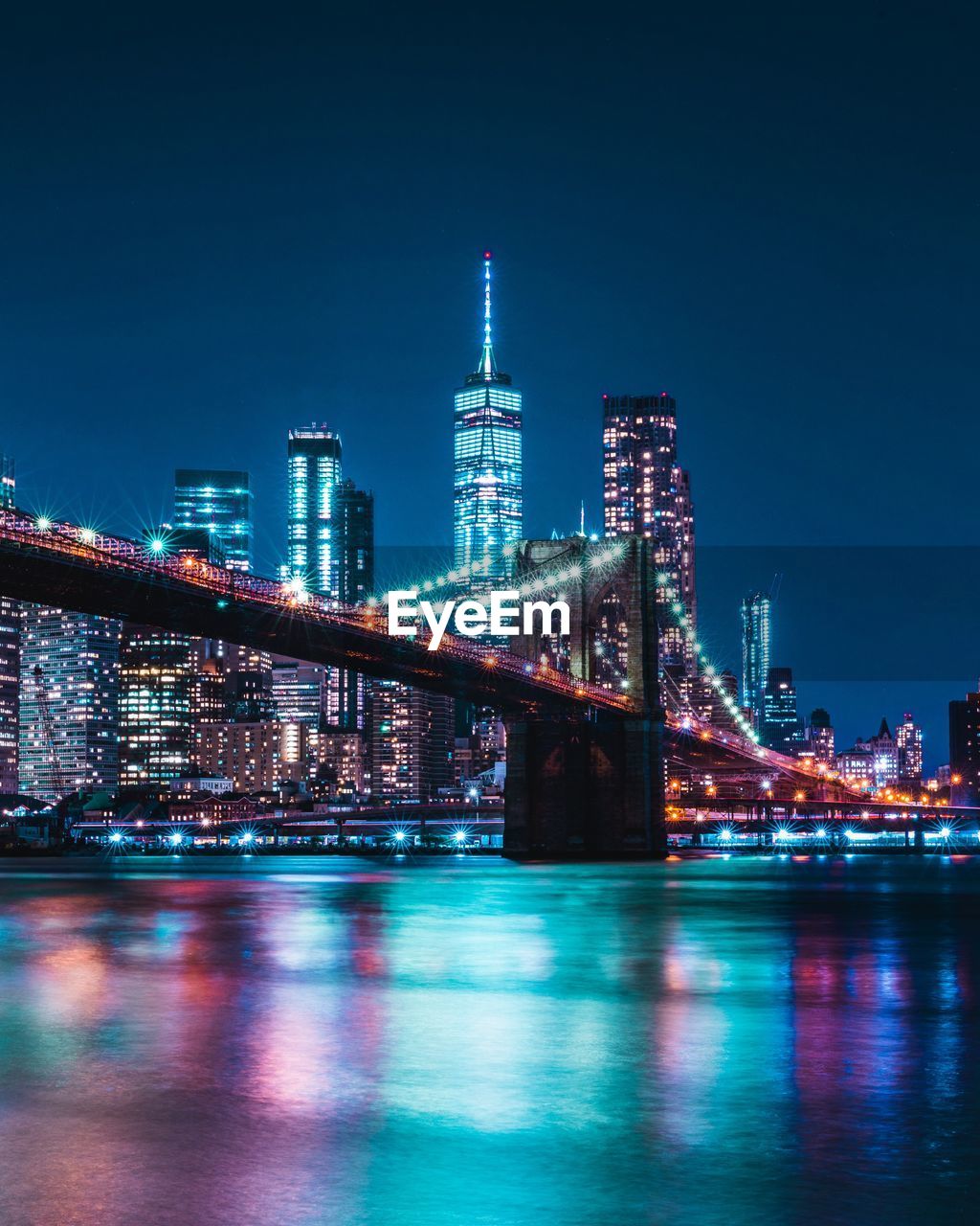 Illuminated buildings by river against sky at night