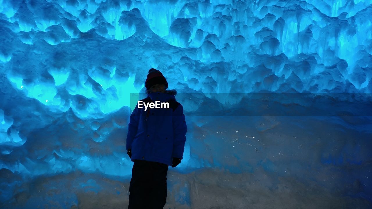 Boy wearing warm clothing standing in ice cave