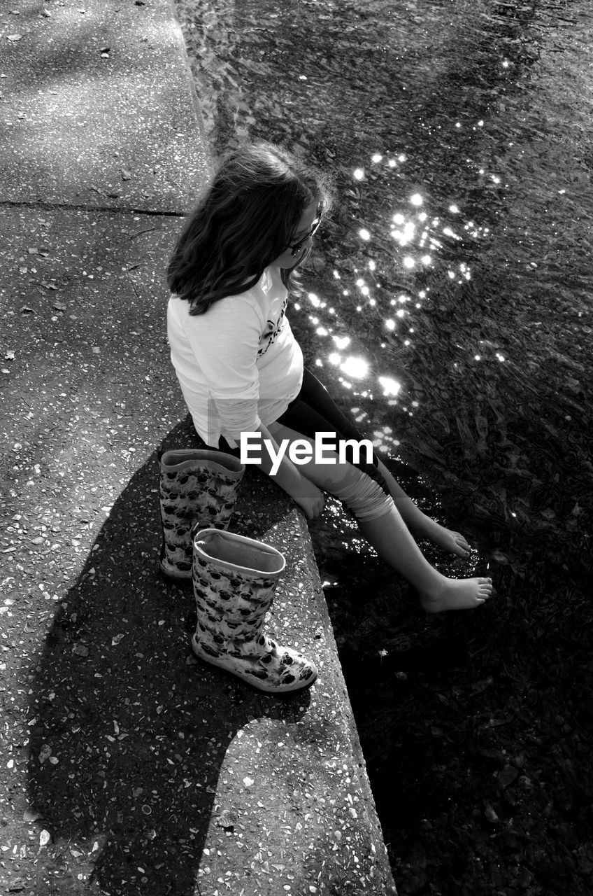 High angle view of girl sitting on retaining wall by river