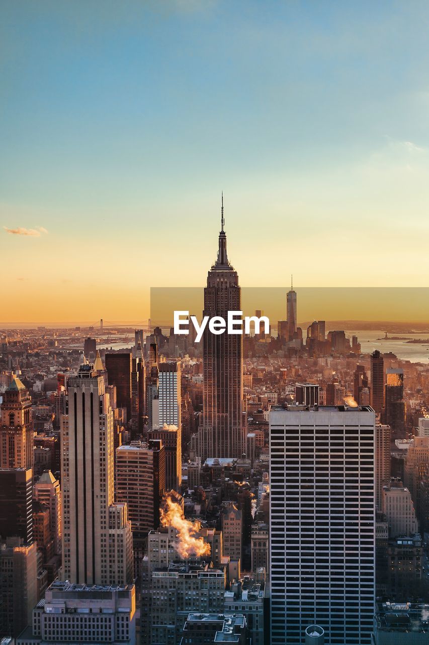 Illuminated empire state building and cityscape against sky during sunset