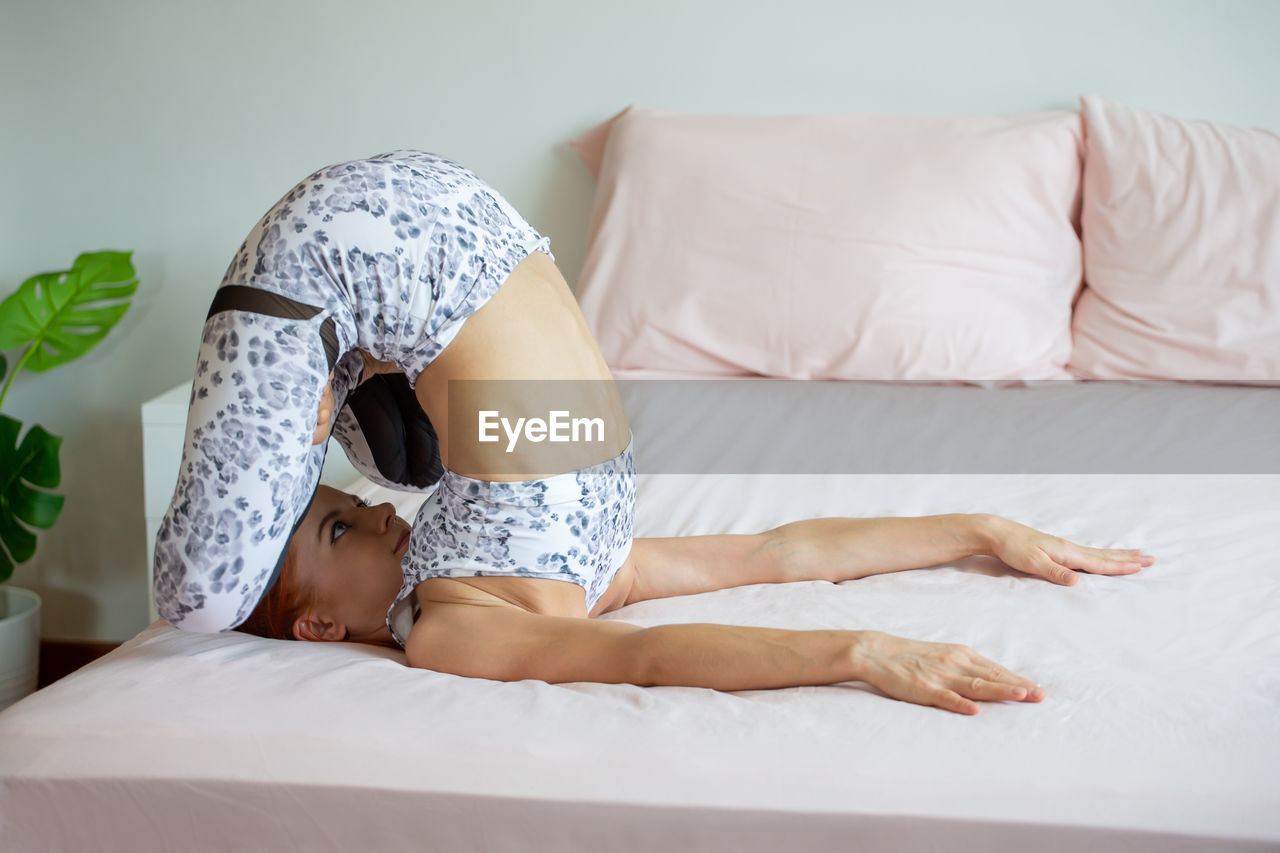 Woman doing yoga on bed at home
