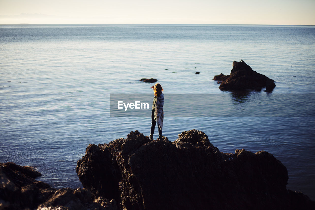 MAN STANDING ON ROCK AGAINST SEA