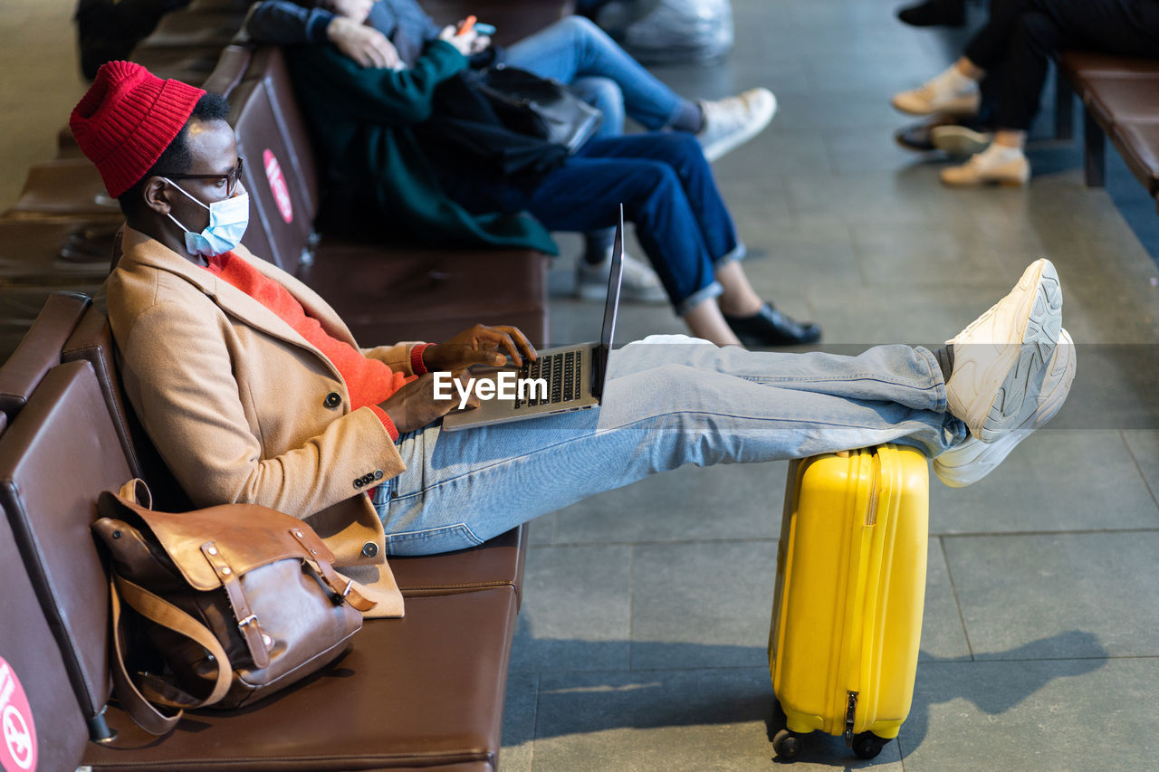 Young businessman wearing mask using laptop while sitting at airport