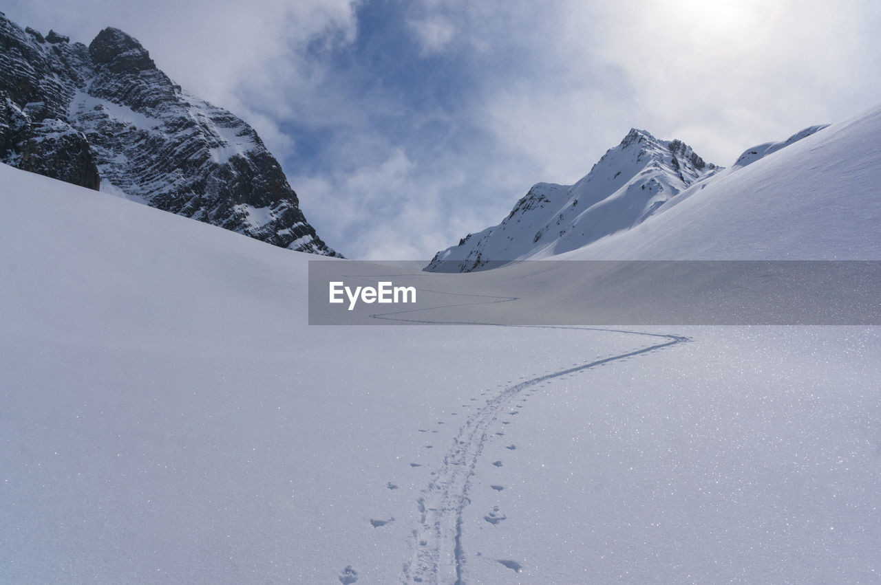 Ski track on snowcapped mountain against sky