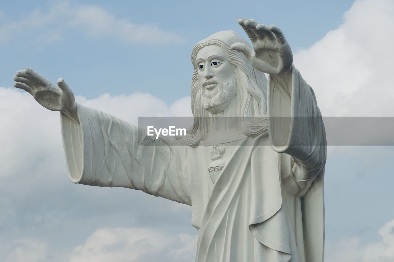 Standing majestic jesus statue blessing with both the hands against blue sky background.