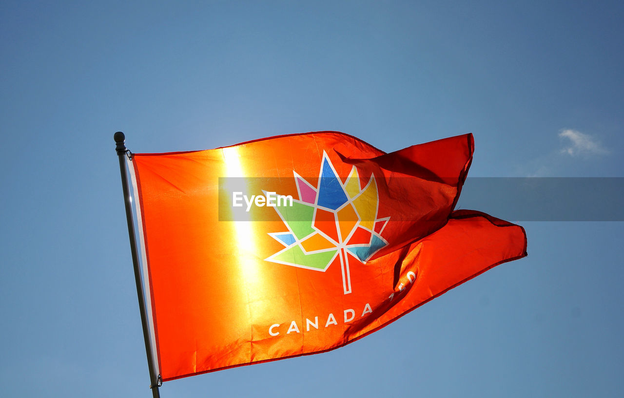 Low angle view of orange flag against blue sky