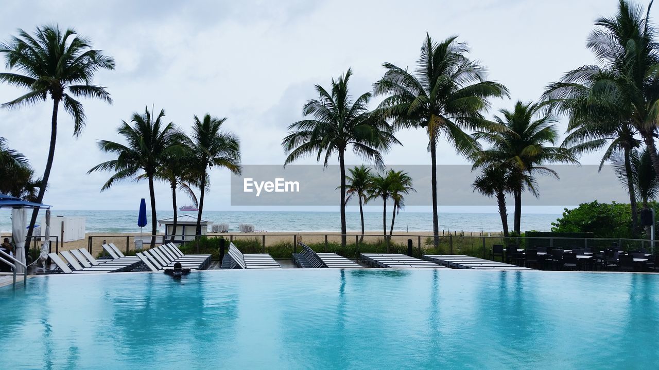 Swimming pool by deck chairs at resort on beach against sky