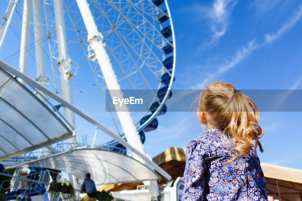 REAR VIEW OF WOMAN IN AMUSEMENT PARK AGAINST SKY