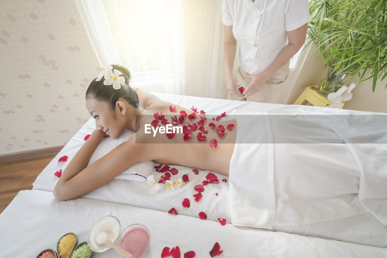 Shirtless young woman with rose petals lying on massage table at spa