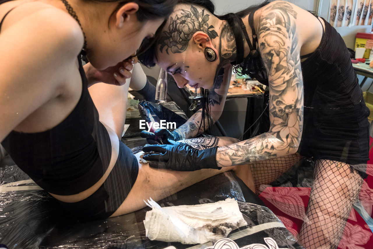 adult, tattoo, young adult, women, tattooing, two people, limb, person, lifestyles, body adornment, men, indoors, clothing, creativity, female, togetherness, fashion