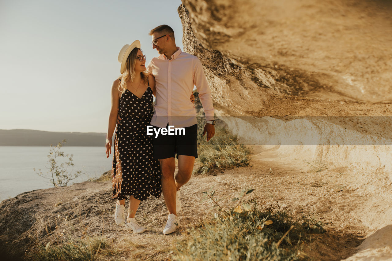 Couple walking on rock formation during sunset