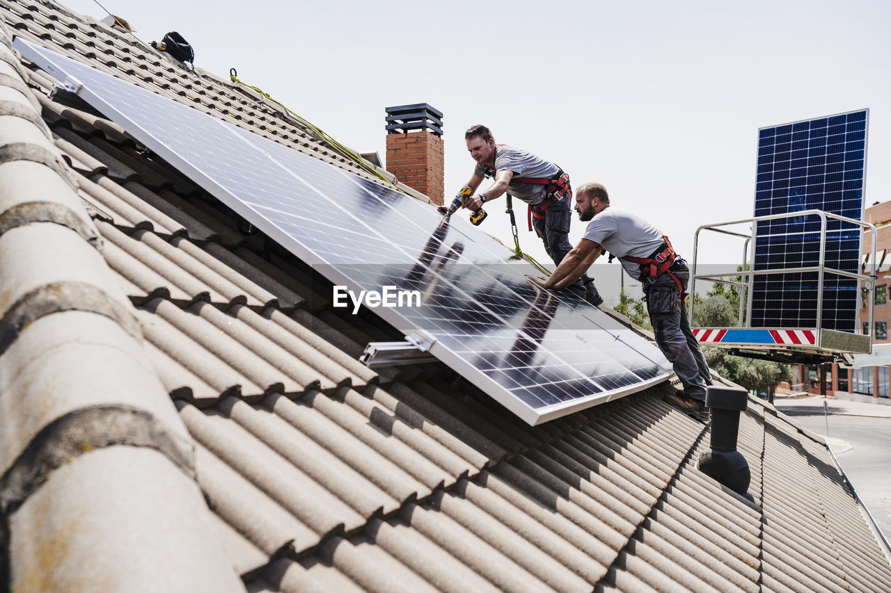 Craftsmen installing solar panels on rooftop of house