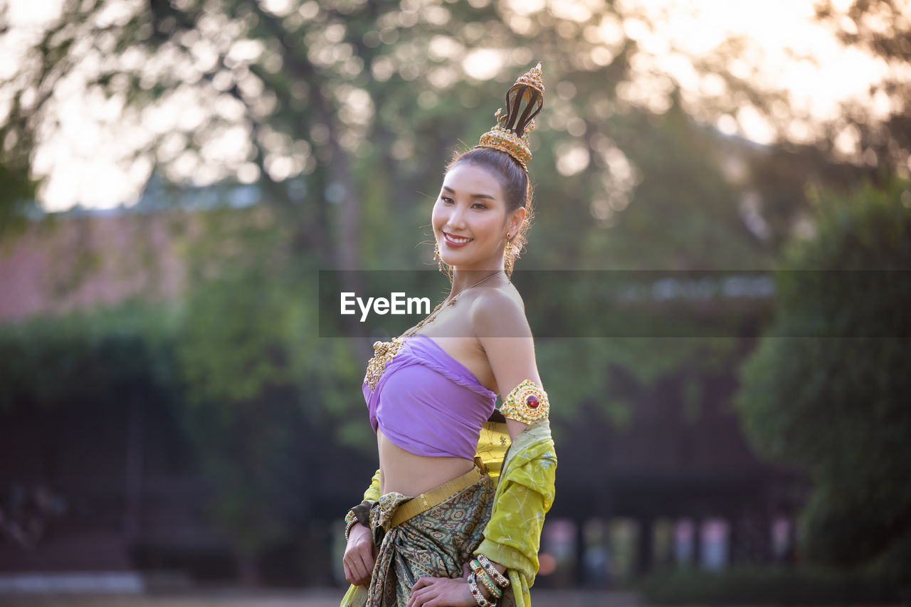 Smiling woman with headdress standing against house