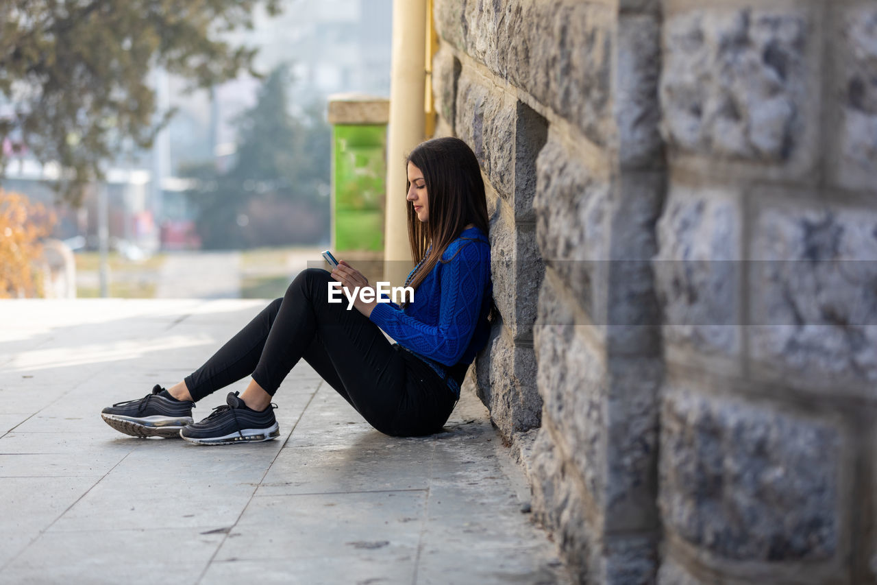 Teen girl sitting on the floor, talking on mobile smart phone, texting and surfing the net