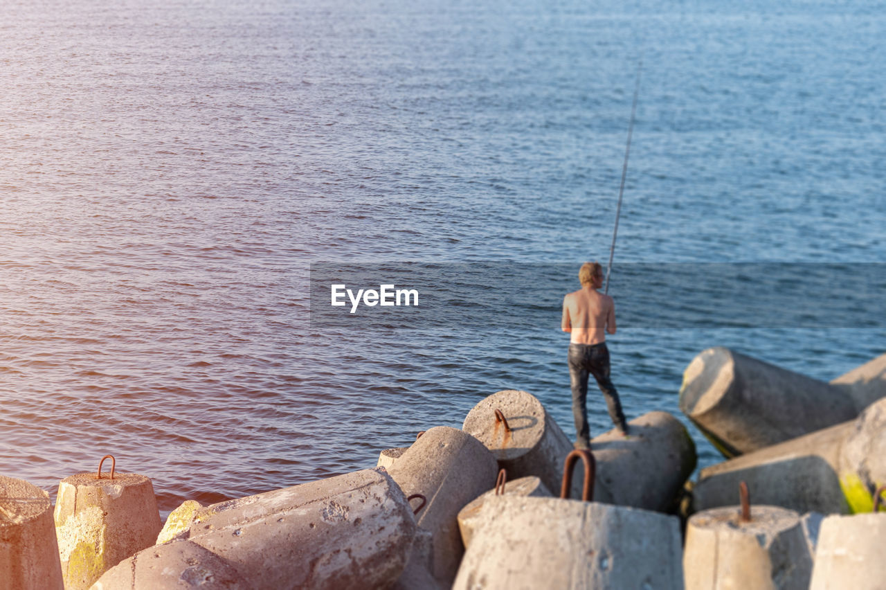 REAR VIEW OF MAN FISHING AT SEA