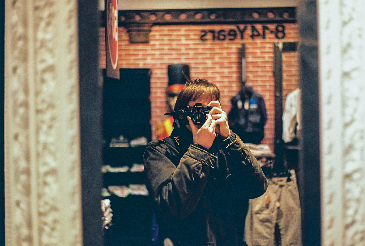 MIDSECTION OF WOMAN PHOTOGRAPHING WITH CAMERA ON SIDEWALK