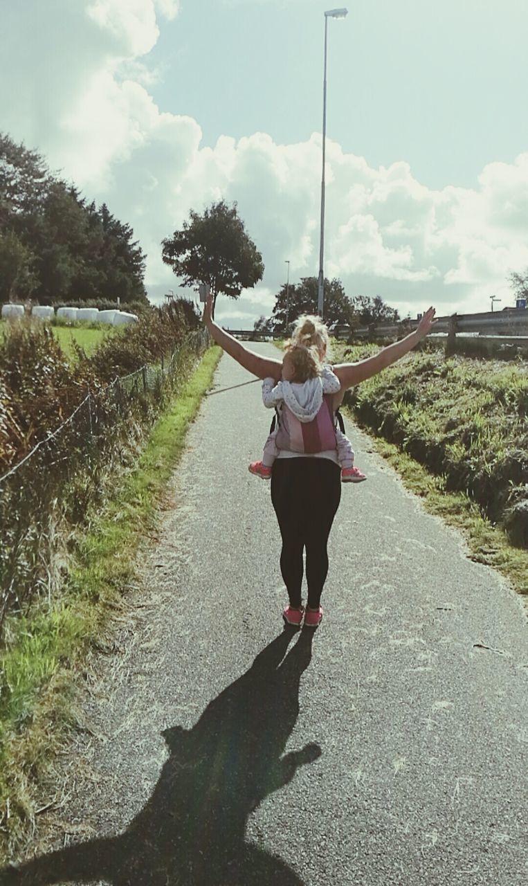 REAR VIEW OF WOMAN WALKING ON FOOTPATH ALONG TREES