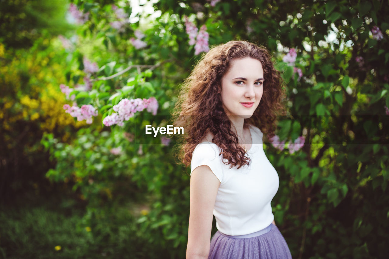 Cheerful young woman in a white t-shirt under the blooming trees. spring park with lilac