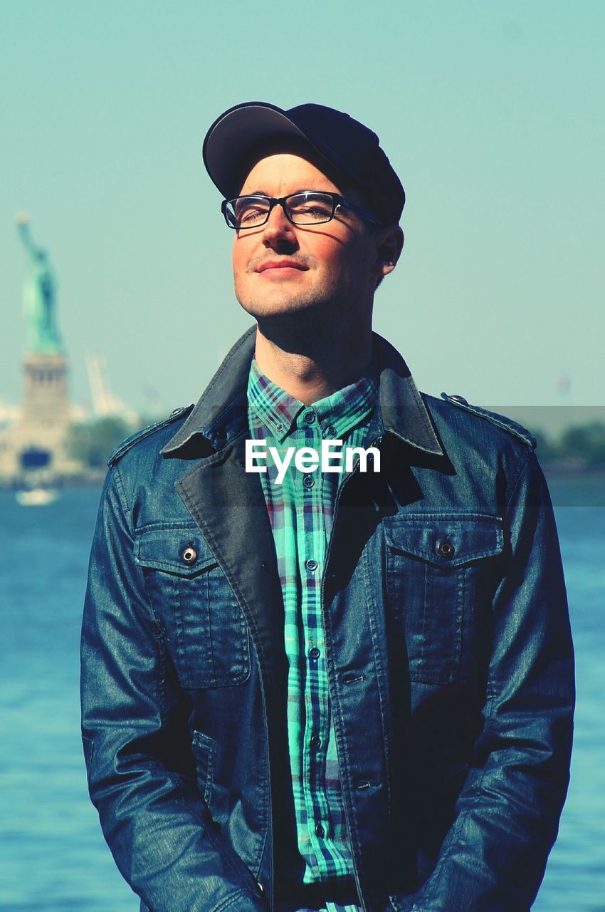 Smiling mid adult man with eyes closed standing against river in city during sunny day