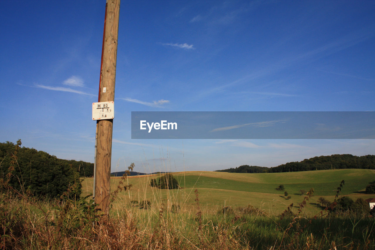 Placard on wooden post at field against sky