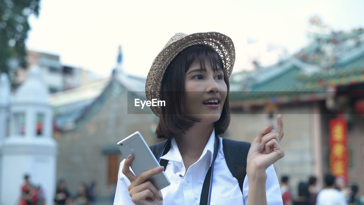 Smiling woman looking away while holding mobile phone in city