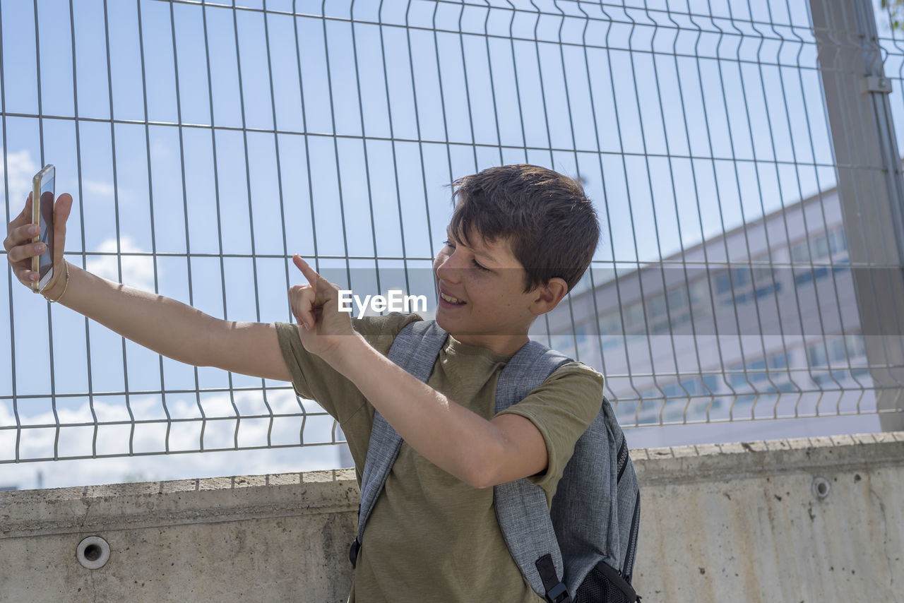 Teenage boy taking selfie by fence