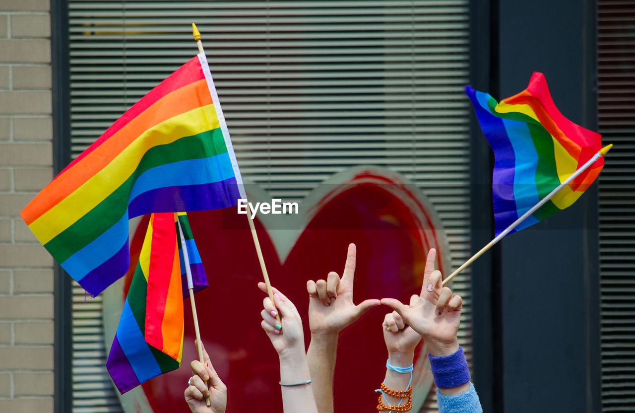 Cropped hands of women holding rainbow flags in city