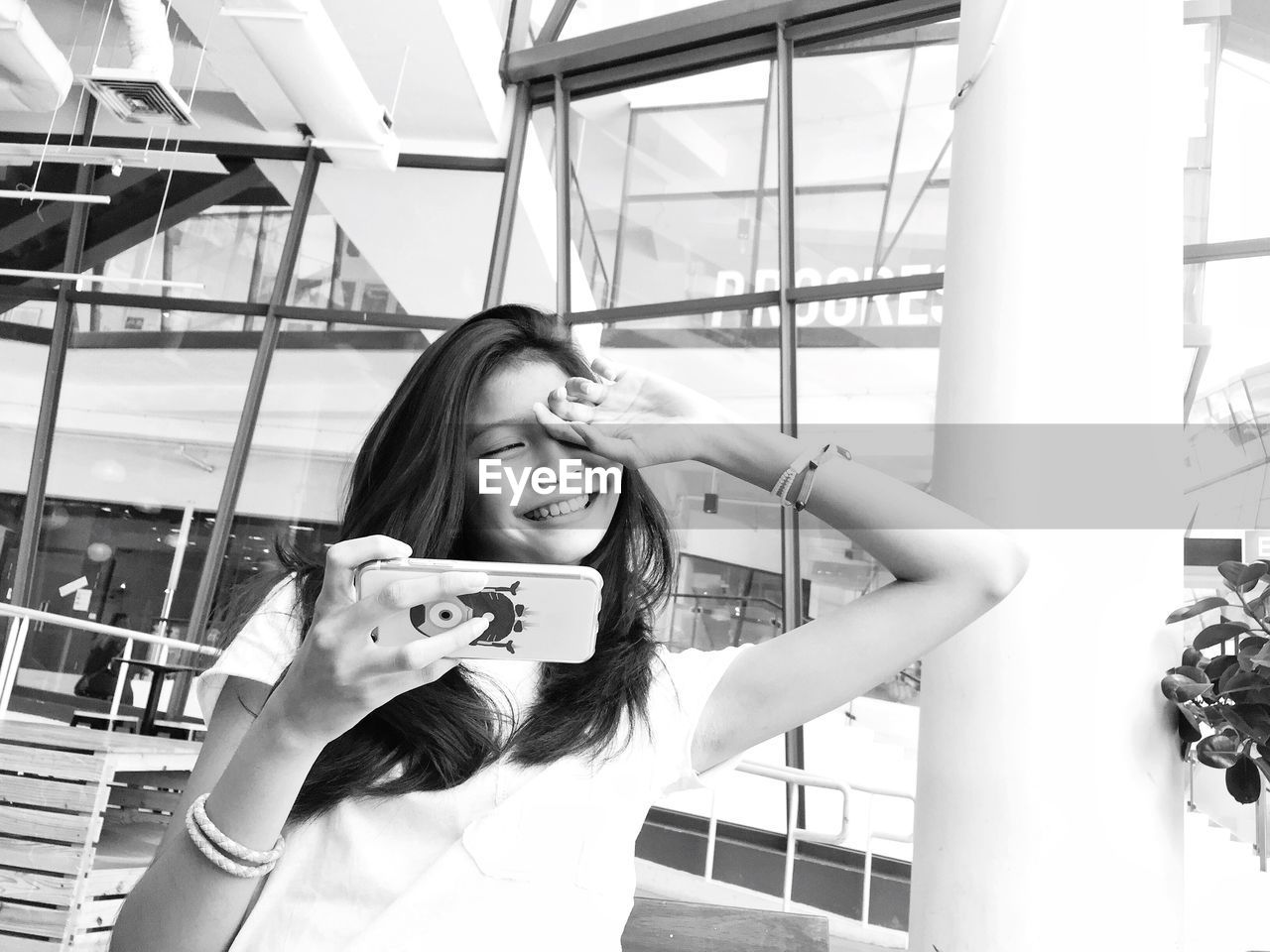 Young woman with hand over eye holding smart phone standing outdoors