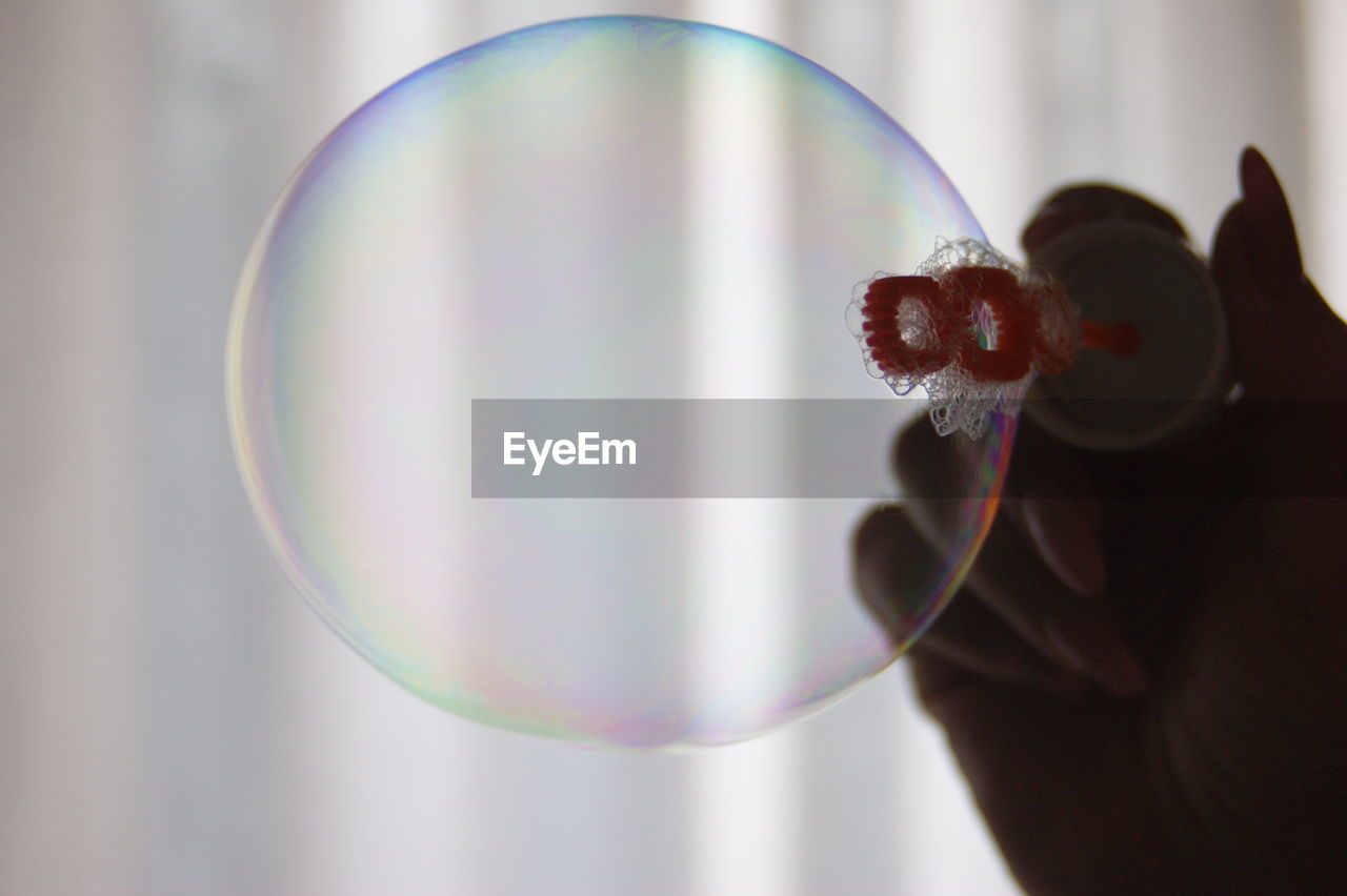 Cropped image of woman holding bubble wand against curtain