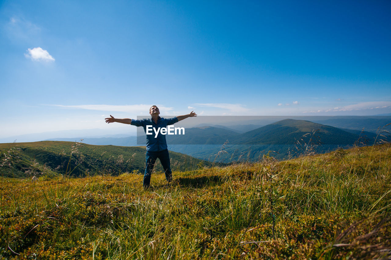 Man with arms outstretched on field against sky