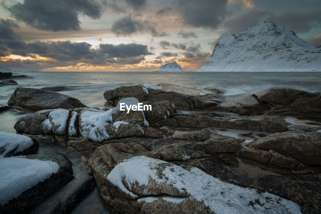 Scenic view of sea by snowcapped mountains against sky during sunset